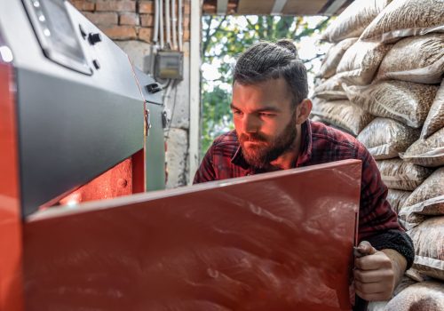 The young man looking into a solid fuel boiler, working with biofuels, economical heating.